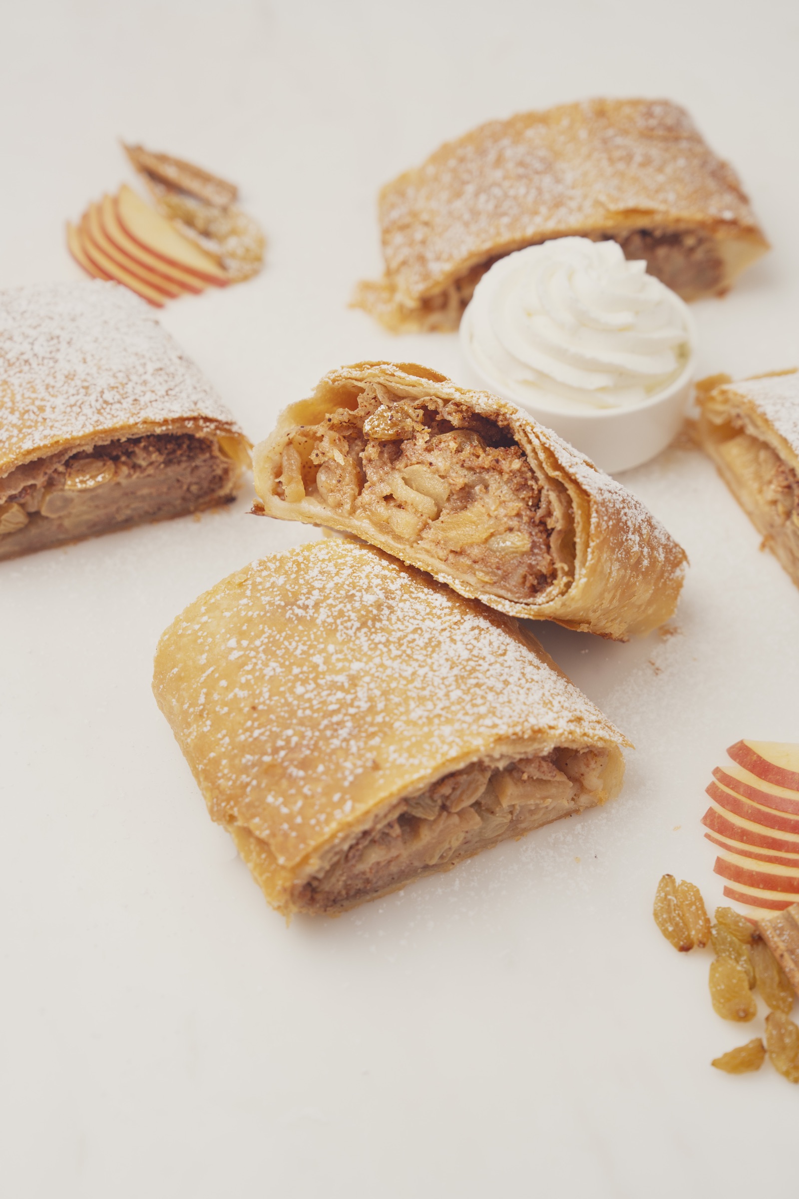 Sliced apple strudel dusted with icing sugar and served with whipped cream